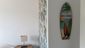 Un dormitorio con cama, mesita de noche, lámpara, puerta y pared decorada con una tabla de surf.