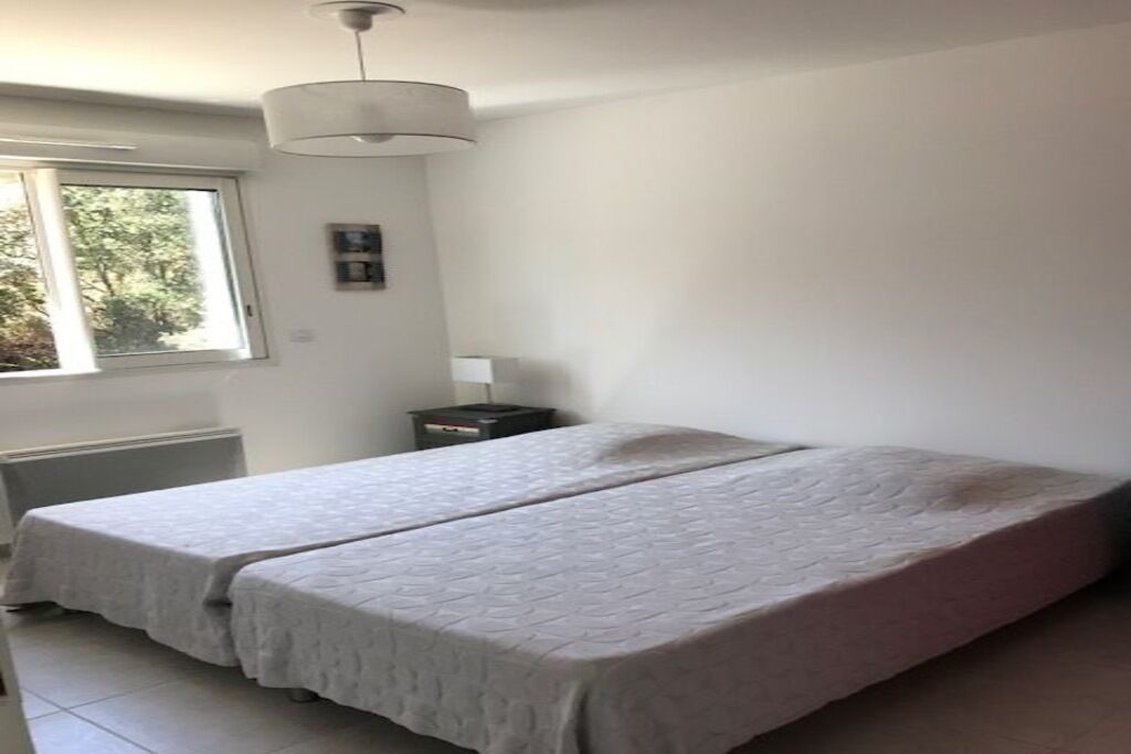 A room with two beds, a window, a heater, and a small table with a lamp.