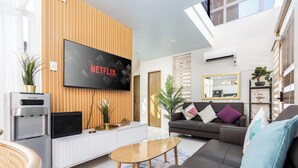 Ein modernes Wohnzimmer mit Flachbildfernseher, Wasserspender, Sofa, Couchtisch und einem großen Spiegel.