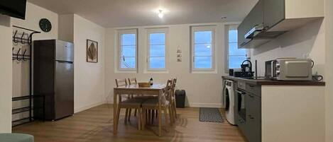 A compact kitchen with a dining area, a TV mounted on the wall, and a refrigerator.