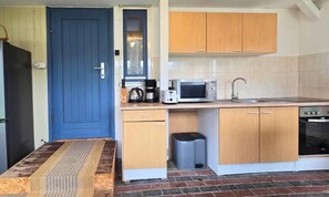 A compact kitchen with wooden cabinets, a microwave, a coffee maker, and a trash bin. - Bungalow in Schlowe Am See (Borkow)