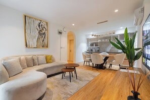A modern living room with a sofa, coffee table, and dining area. - Aima Apartments  (Lekki)