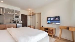 A modern bedroom with a bed, a desk, a TV, and a kitchenette. - Aima Apartments  (Lekki)