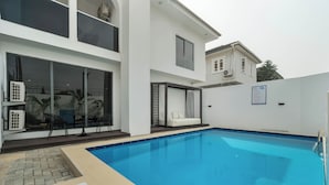 A modern two-story house with a swimming pool, outdoor seating, and a covered patio area. - Aima Apartments  (Lekki)