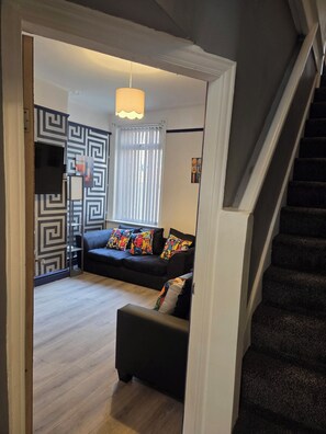 Ein Wohnzimmer mit einer schwarzen Couch, bunten Kissen, einer Wand mit Muster und einer Treppe.