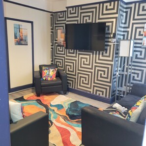A room with a patterned wall, a flat-screen TV mounted above a black leather chair, a colorful rug, and a sofa with a patterned cushion. - 4 bedroom house with a 5 minute walk to Anfield, home of Liverpool F.C. (Liverpool)
