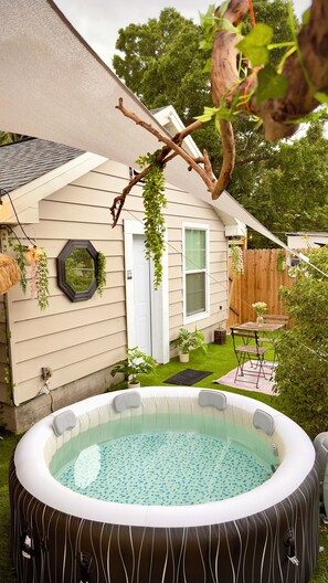 Un patio trasero con jacuzzi, cubierta de madera, una casa con puerta y cerco.