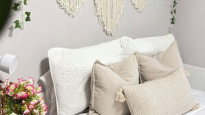 Une chambre avec un lit, une décoration murale en macramé et des plantes suspendues.