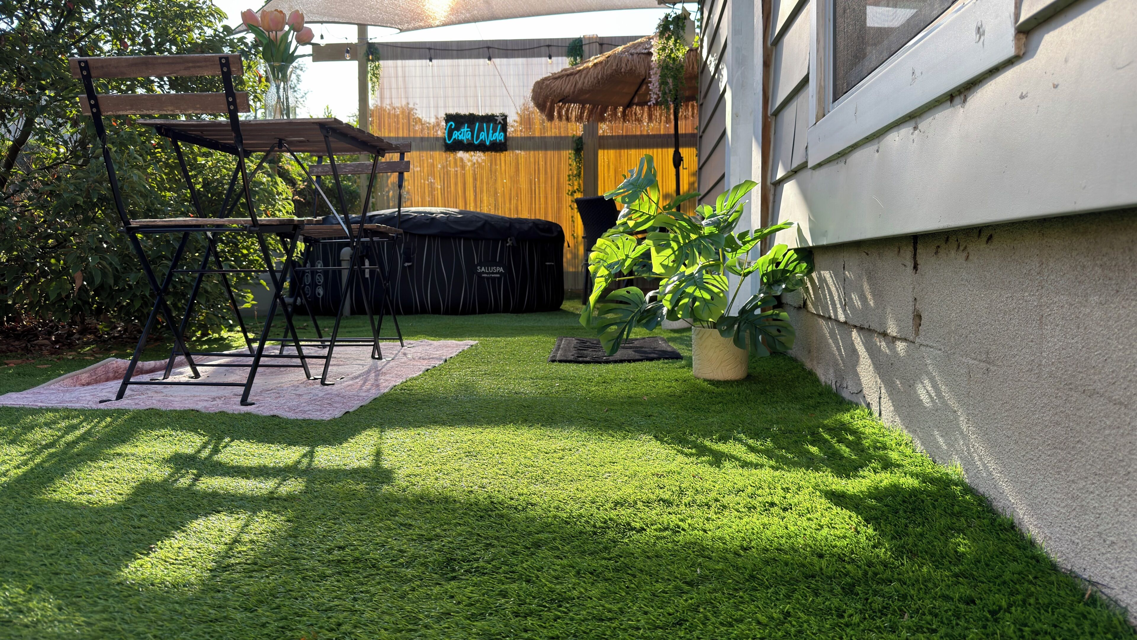 Un patio con una mesa y sillas de madera, un sofá negro y una planta en maceta.