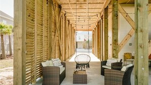 A covered outdoor seating area with wicker furniture and a hanging chair, connected by a wooden structure. - Unit 028 - Sea Goodness (Dauphin Island)