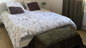Une chambre à coucher avec un lit, deux oreillers, une table de chevet, une lampe et une fenêtre avec des rideaux.