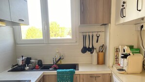 Une cuisine compacte avec des meubles en bois, un four encastré, un évier et une fenêtre qui laisse entrer la lumière naturelle.