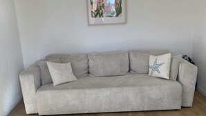 Un salon avec un canapé gris, une estampe botanique encadrée au mur et une petite table accompagnée de deux chaises.