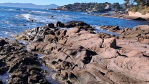 Un littoral rocheux bordé d’une eau d’un bleu limpide et dominé par des collines lointaines.