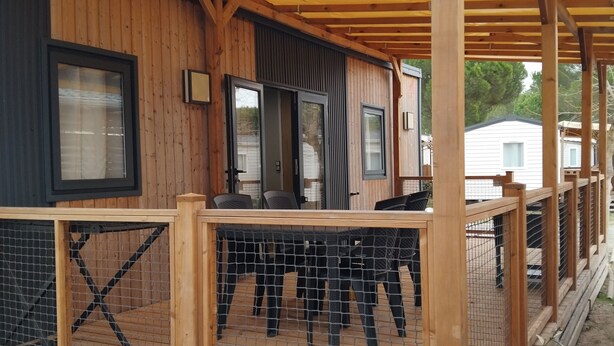 Eine Holzhütte mit überdachter Veranda, ausgestattet mit einem umzäunten Deck mit Stühlen und einem Tisch.