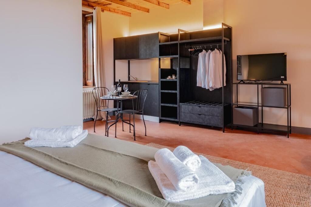 A hotel room with a bed, a dining table with chairs, a TV, a wardrobe, and a small seating area.