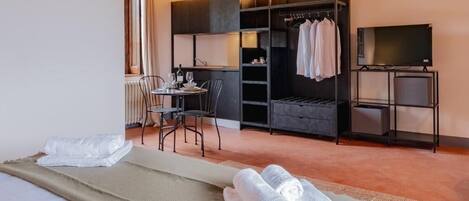 A hotel room with a bed, a dining table with chairs, a TV, a wardrobe, and a small seating area.