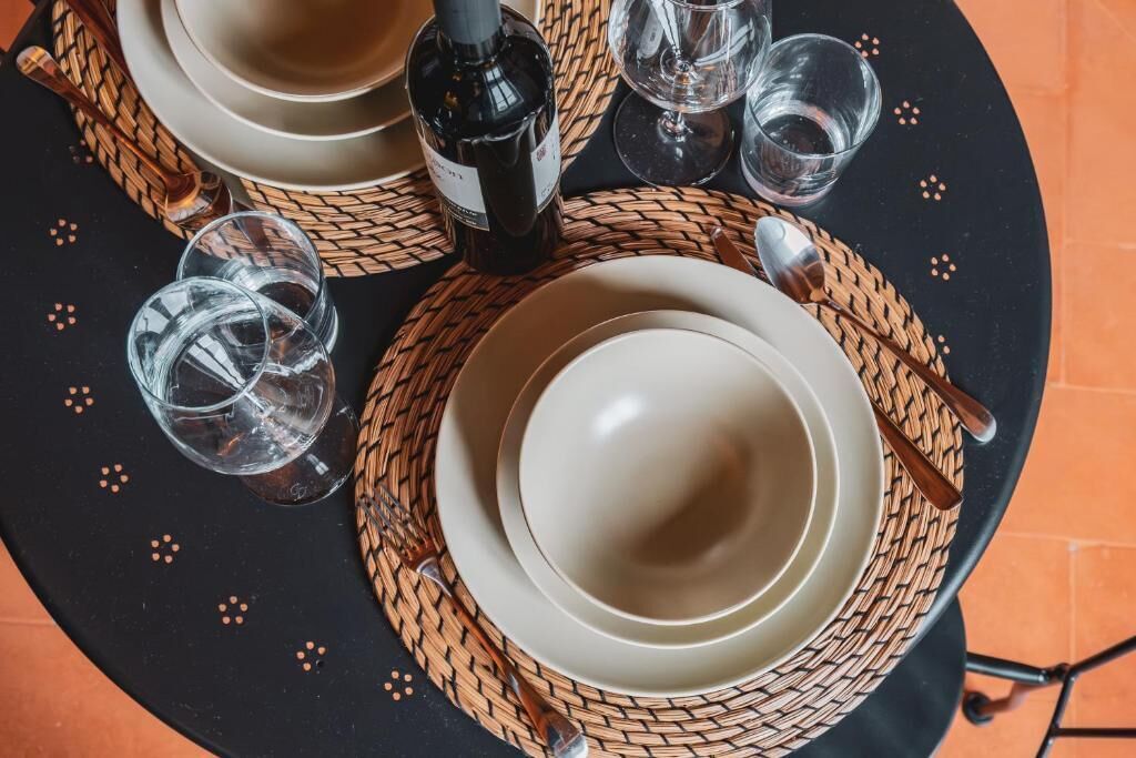 A table set with plates, glasses, a bottle, and cutlery on a woven placemat.