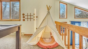 Una habitación con suelo de madera, una mesa de madera, una estructura parecida a una tienda con cojines y una escalera.