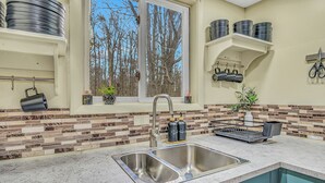 Una cocina con un lavamanos doble, una ventana con vistas a árboles y un salpicadero con diseño de mosaico.