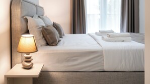 Una cama bien hecha con sábanas blancas, una lámpara de noche y un arreglo de almohadas en la cabecera.