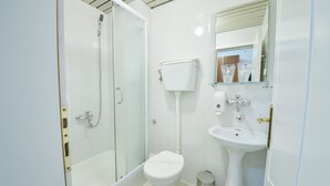 Un baño pequeño con inodoro, lavabo y ducha con mampara de cristal.