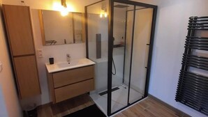 Un baño moderno con ducha envuelta en vidrio, tocador de madera y un espejo grande.