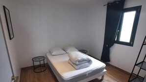 Un dormitorio pequeño y bien iluminado con una cama individual, una mesita y una ventana con cortinas.