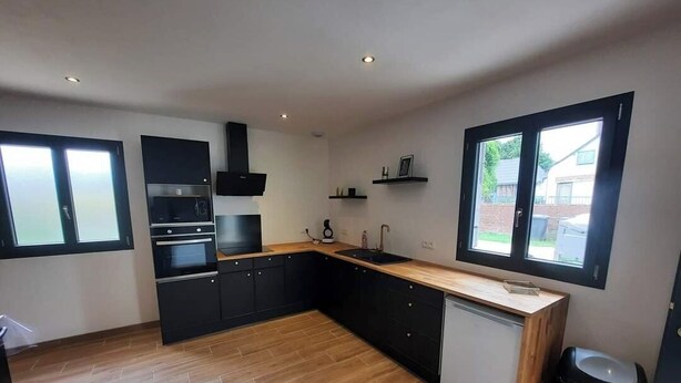 Una cocina moderna con armarios negros, encimera de madera y lavavajillas integrado.