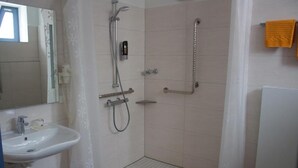 Une salle de bain avec un lavabo blanc, une douche équipée d’un pommeau de douche à main et un porte-serviettes sur lequel est posée une serviette jaune.