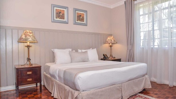 Un dormitorio ordenado con una cama grande, dos mesitas de noche con lámparas, una mesita de madera, una alfombra roja estampada y dos cuadros en la pared.