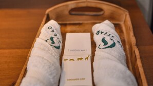 Una bandeja de madera con dos toallas blancas y una caja etiquetada como 'Sanitary Bag' en un baño.