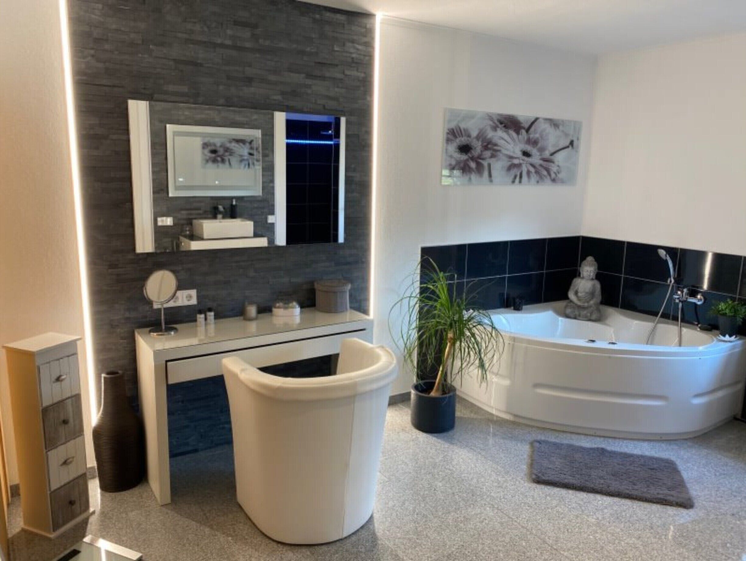 A modern bathroom with a vanity, a large mirror, a sink, a toilet, a bathtub, and a potted plant.