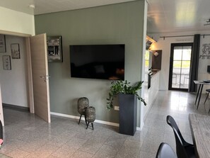 A modern living room with a flat-screen TV mounted on the wall, a small side table, and a potted plant.