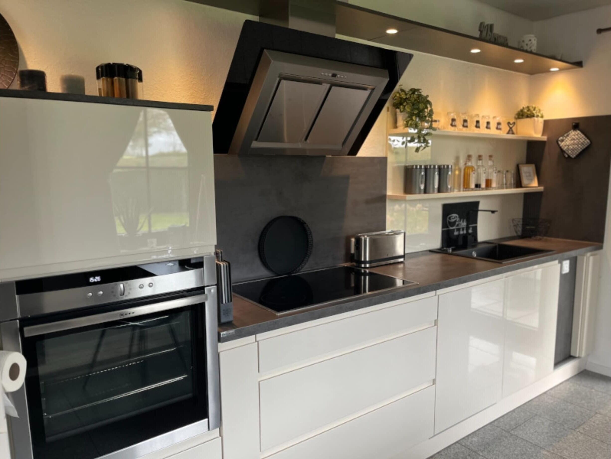 A modern kitchen with a built-in oven, a stovetop, and a range hood. There are cabinets and a countertop with various kitchen items.