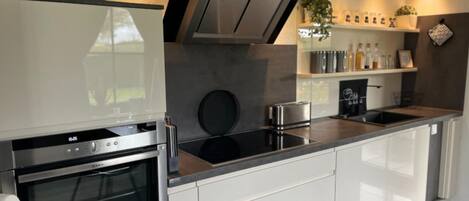 A modern kitchen with a built-in oven, a stovetop, and a range hood. There are cabinets and a countertop with various kitchen items.