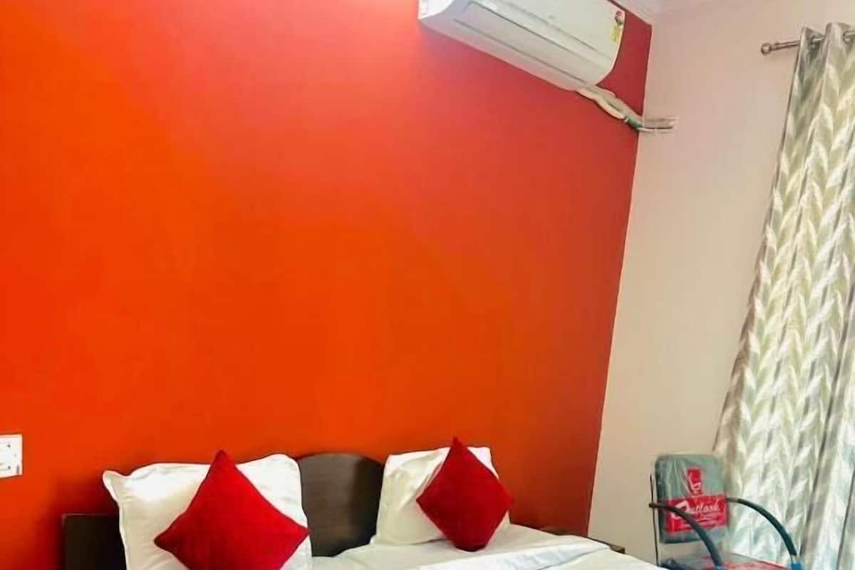 Ein Hotelzimmer mit Bett, roten Kissen, einer weißen Bettdecke und einer an der Wand montierten Klimaanlage.