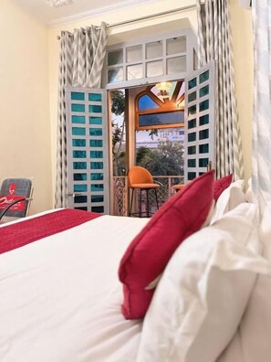 A hotel room with a bed, a red pillow, a chair, and a window with curtains. - Angel paradise (Jaipur)