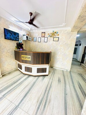 A reception area with a marble floor, a reception desk labeled 'RECEPTION,' a ceiling fan, and framed pictures on the wall. - Angel paradise (Jaipur)