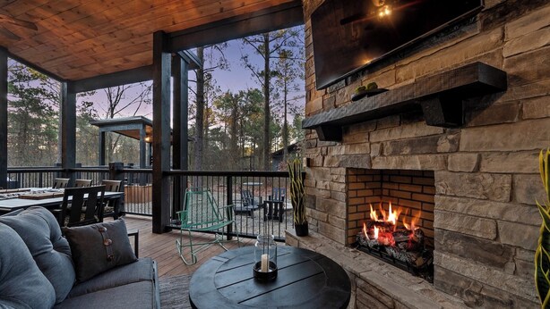 An outdoor patio with a stone fireplace, a wooden ceiling, and a view of trees. - 4BR Broken Bow Cabin Sleeps 12 | Hot Tub, Arcade, Firepit (Broken Bow)
