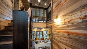 A wooden interior with a staircase leading to a loft bedroom, a sofa set, and a large window. - 4BR Broken Bow Cabin Sleeps 12 | Hot Tub, Arcade, Firepit (Broken Bow)