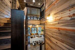Ein Holzinnenraum mit einer Treppe zu einem Schlafzimmer im oberen Bereich, einer Sofagarnitur und einem großen Fenster.