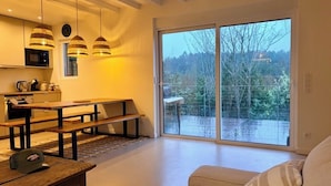 Eine moderne Küche mit Holzbänken, Pendelleuchten und einer großen Schiebeglasdoor, die auf einen Balkon führt.