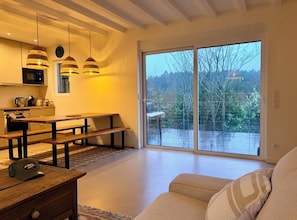 A modern kitchen with wooden benches, pendant lights, and a large sliding glass door leading to a balcony. - Charming new lodge house on the edge of a forest, in a natural setting close to the ocean. (Ondres)