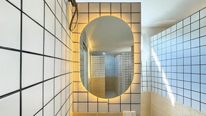A bathroom with a tiled wall, a mirror, and a light fixture. - Nana Best Hostel (Bangkok)