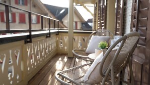 A balcony with wicker chairs and a small table, wooden floor, and a decorative railing.