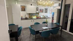 Une cuisine moderne avec des meubles blancs, une table à manger entourée de chaises turquoise et un luminaire sphérique original.