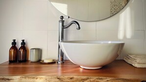 Un baño con un lavabo blanco grande, un espejo y artículos de aseo en la encimera.