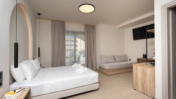Una habitación de hotel moderna con una cama grande, un sofá más pequeño, una mesita de madera, un televisor y vistas a la ciudad.