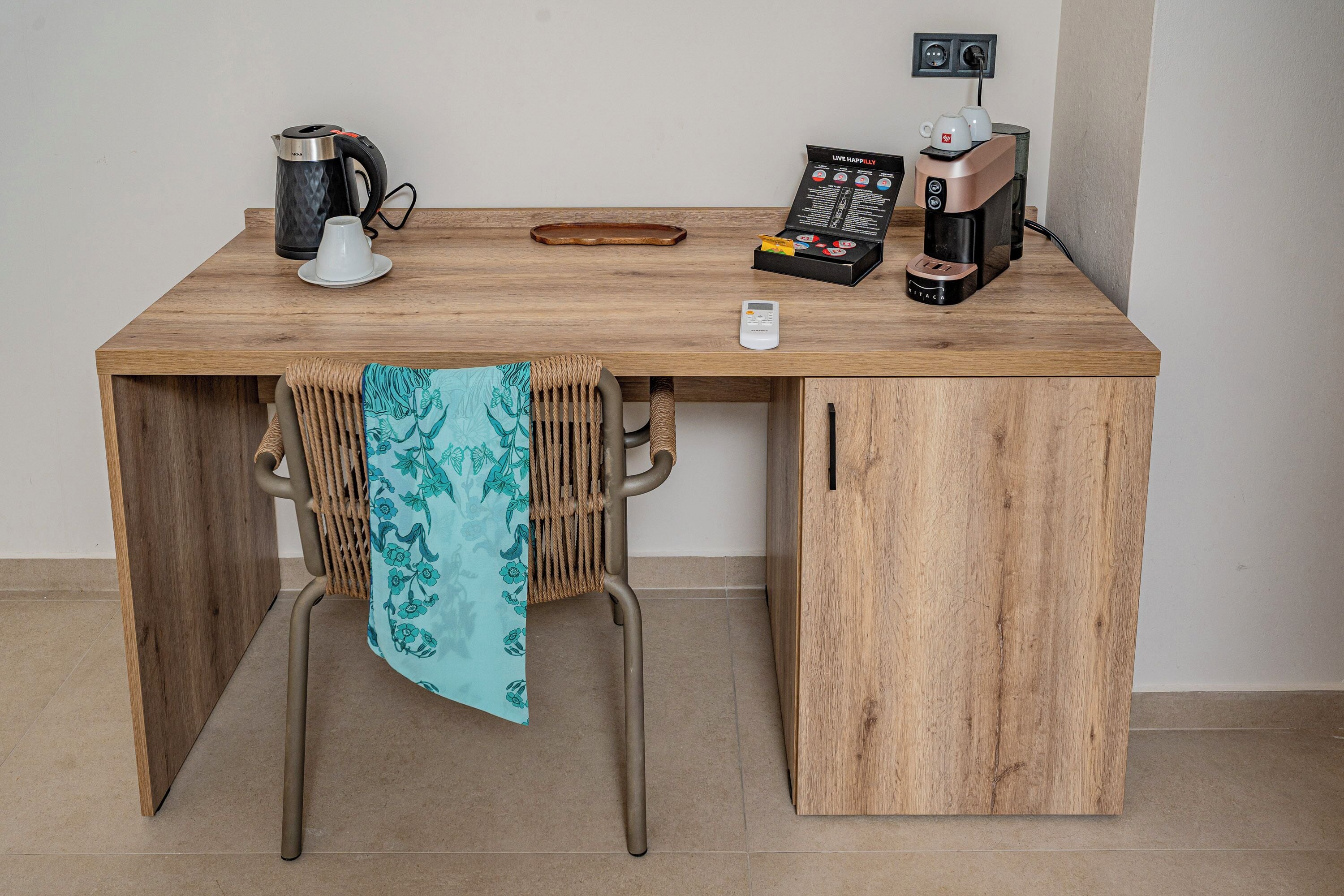 A wooden desk with a coffee maker, a kettle, and a remote control.